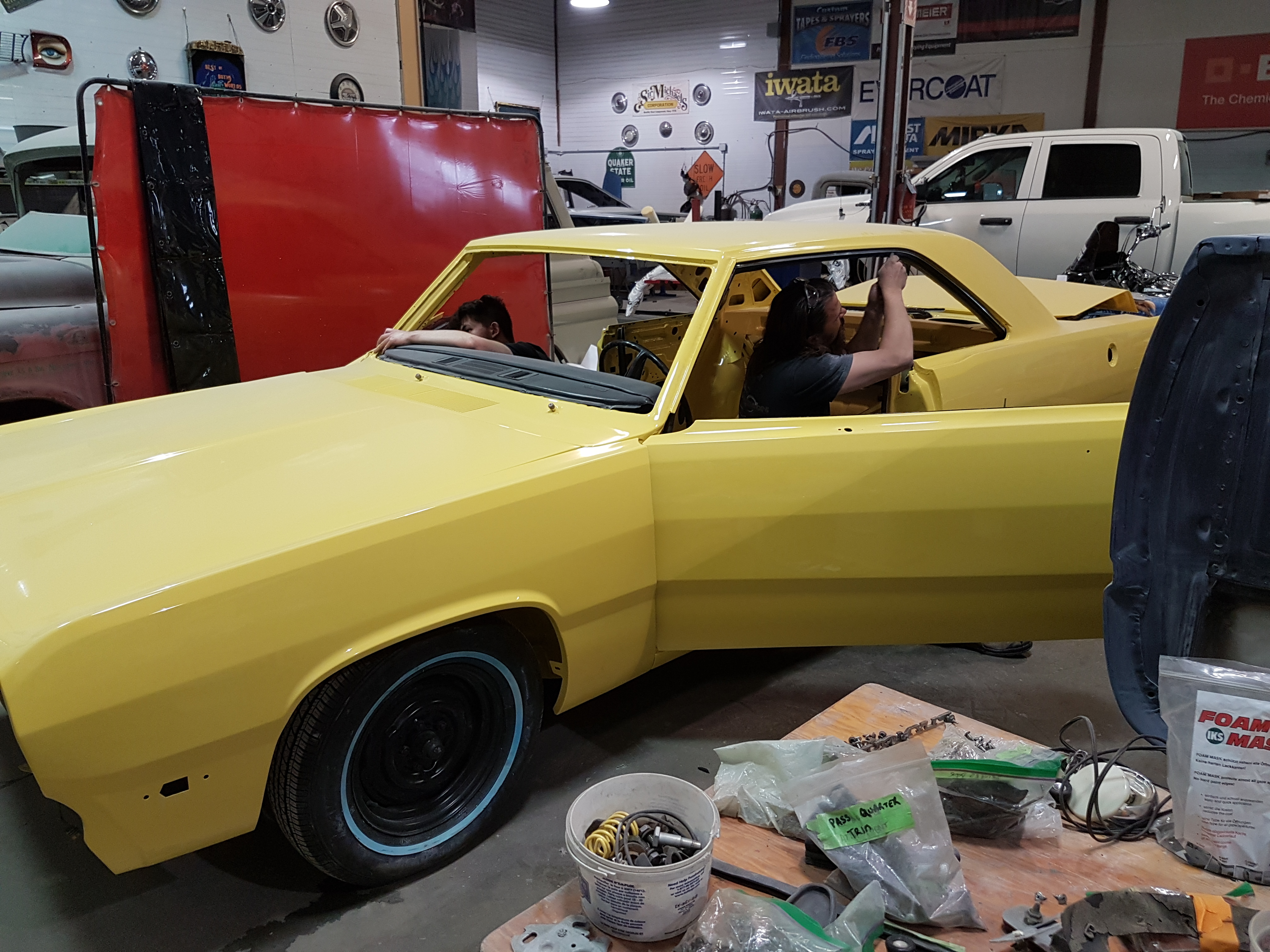 A technician replaces window trim in a yellow 1972 Plymouth Scamp