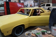 A technician replaces window trim in a yellow 1972 Plymouth Scamp